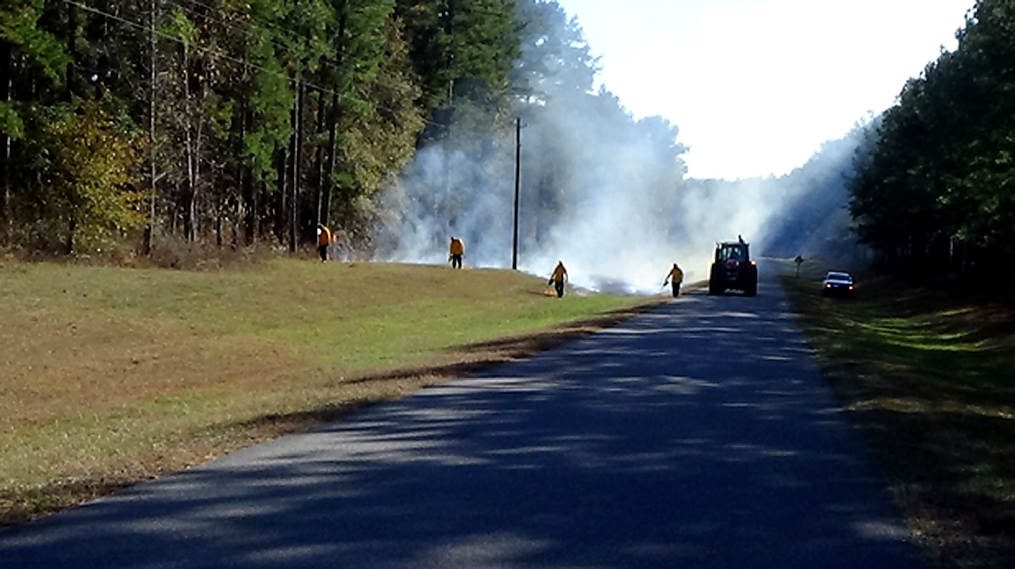 Trained personnel conducting a controlled burn along a paved range road