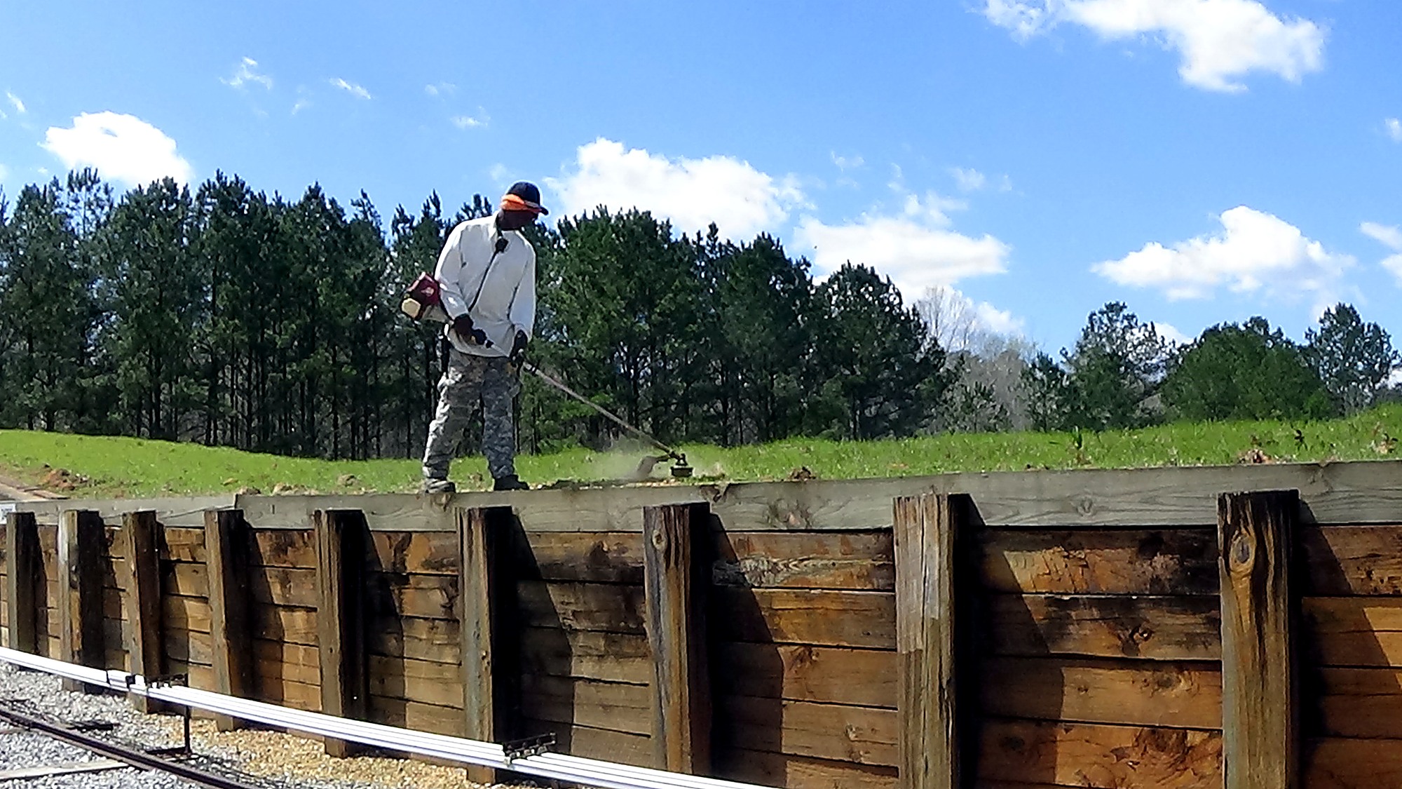Crew member performing vegetation maintenance beside a timber retaining wall